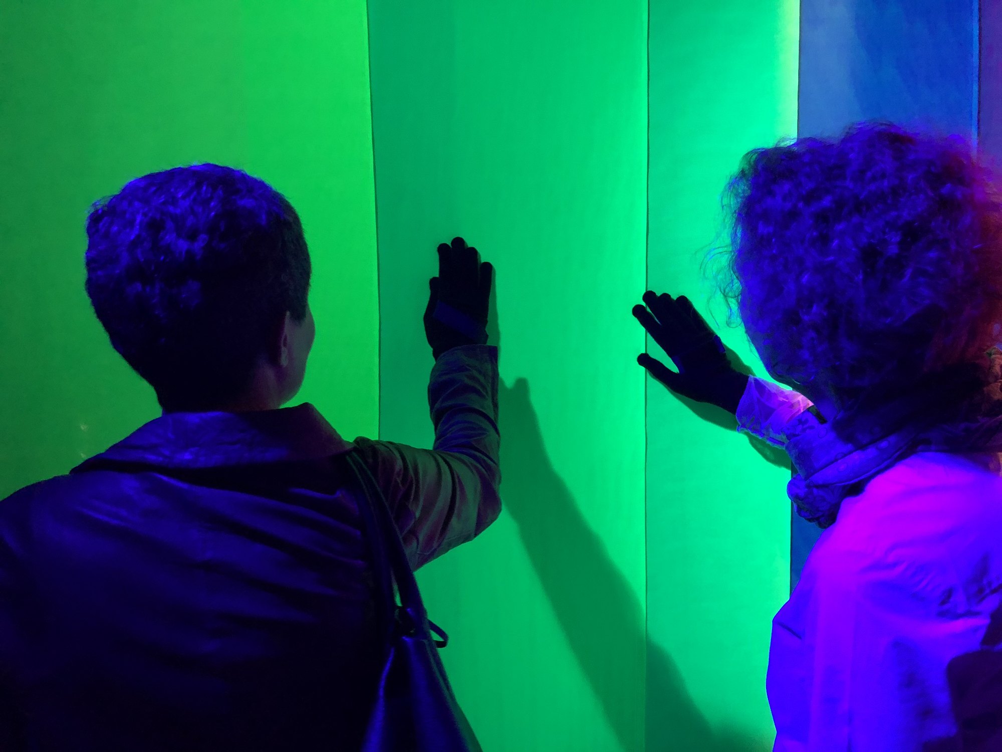 Two visitors on either side of the lit fabric wall, each with a hand on it