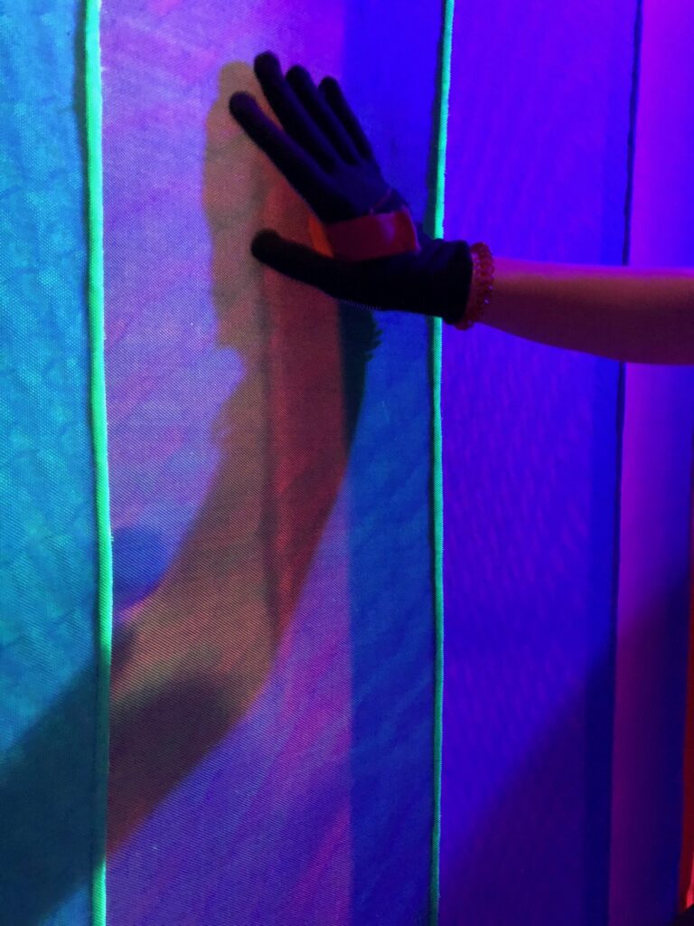 Gloved hand on the fabric wall, lit in blue and purple